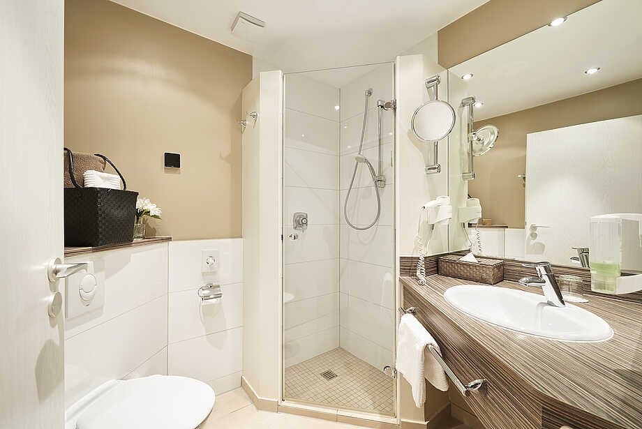 Badezimmer mit Eckdusche, WC, Wachbecken, Fön und Kosmetikspiegel in beigen Farbtönen