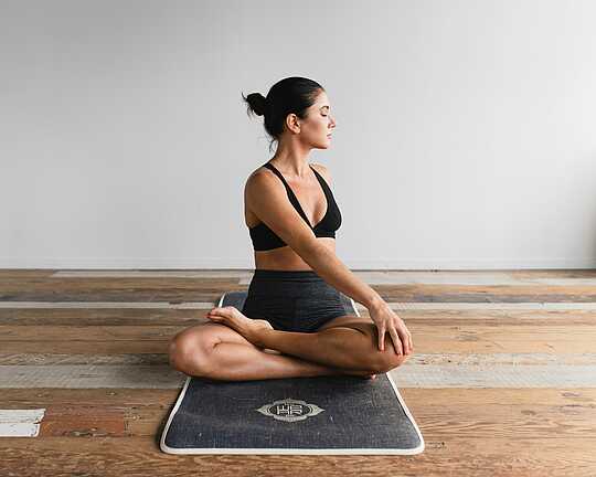 Frau sitzt in Yogapose auf einer Sportmatte