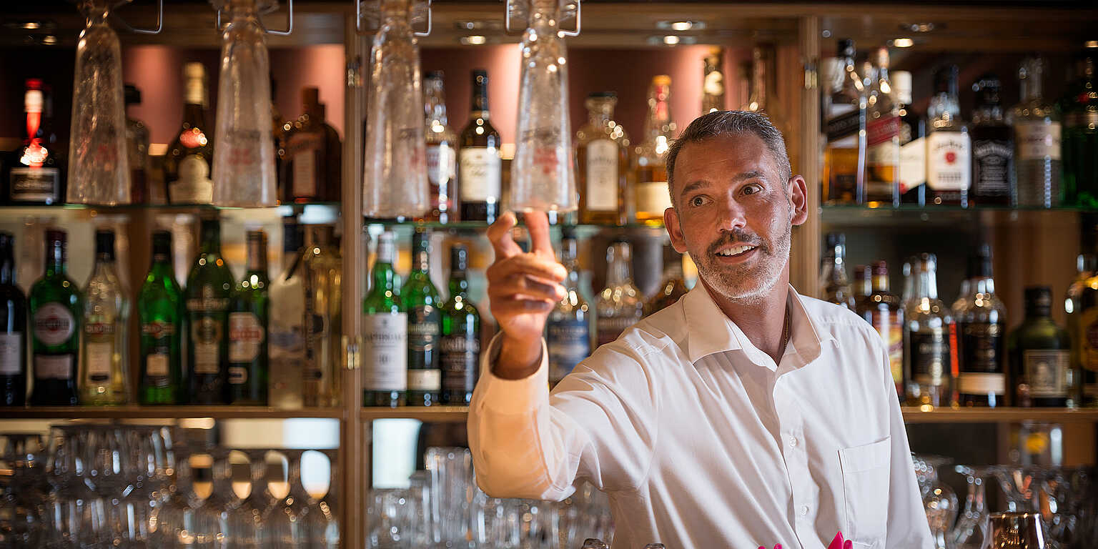 Barkeeper im weißem Hemd greift nach einem Glas