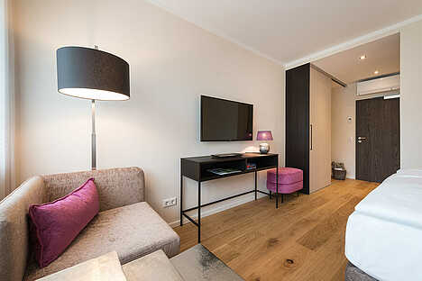 Modernes Hotelzimmer mit einem pinken Hocker und Kissen