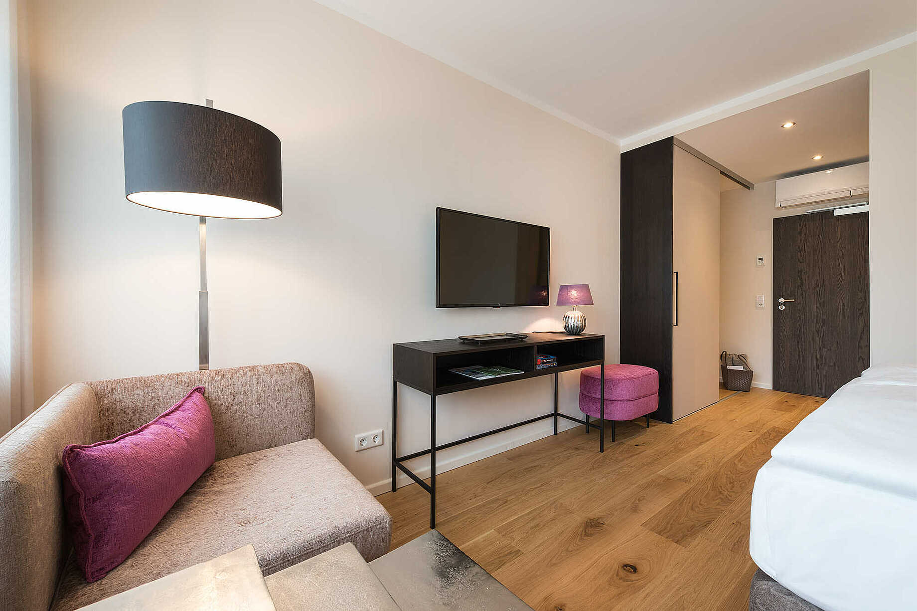 Modernes Hotelzimmer mit einem pinken Hocker und Kissen