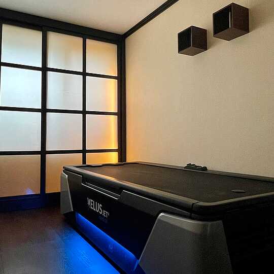 Wasserstrahlmassagenbett mit blauem Lichtstreifen steht in einem Raum mit dunkelbraunem Holzparkett