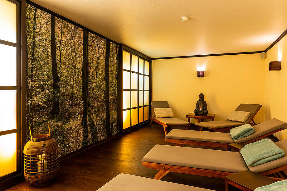 Raum mit Liegen und einer Buddhastatue und Waldbild an der Wand
