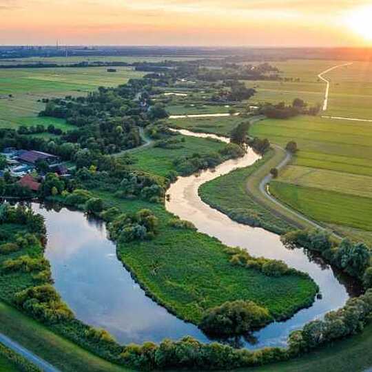 Grüne Wiesenlandschaft mit einem kleinem Fluß bei Sonnenaufgang