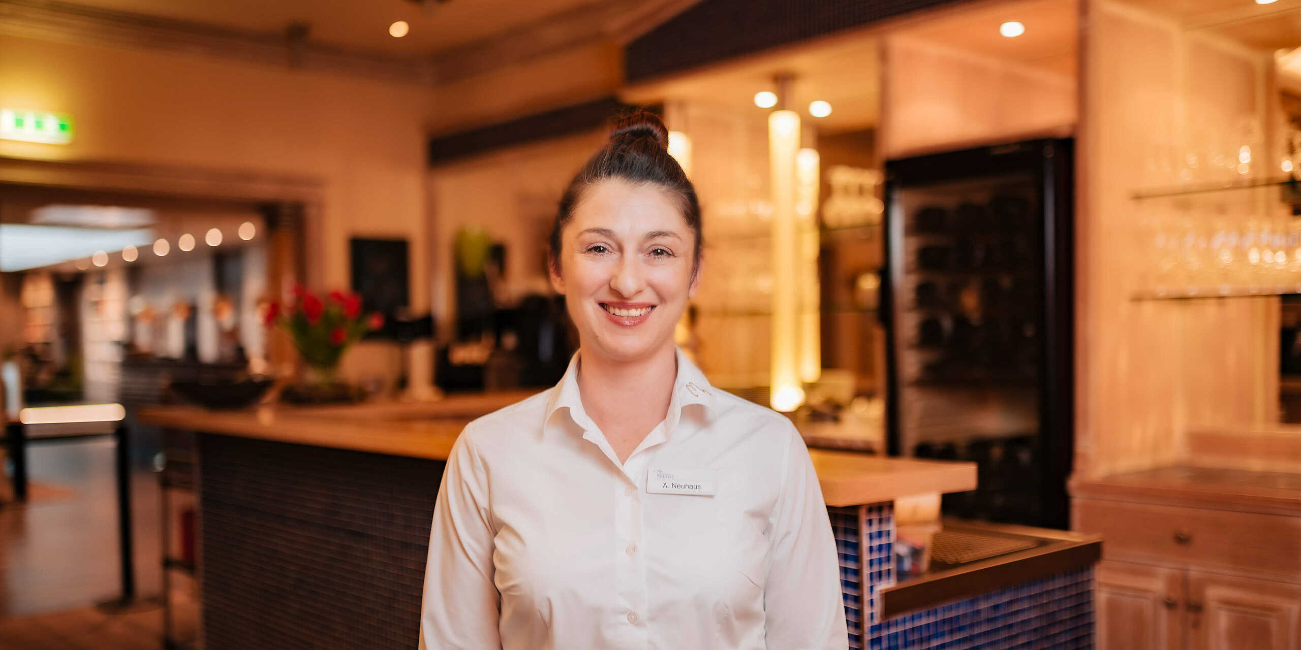Servicemitarbeiterin aus dem Restaurant Wels in weißer Bluse guckt lächelnd in die Kamera 