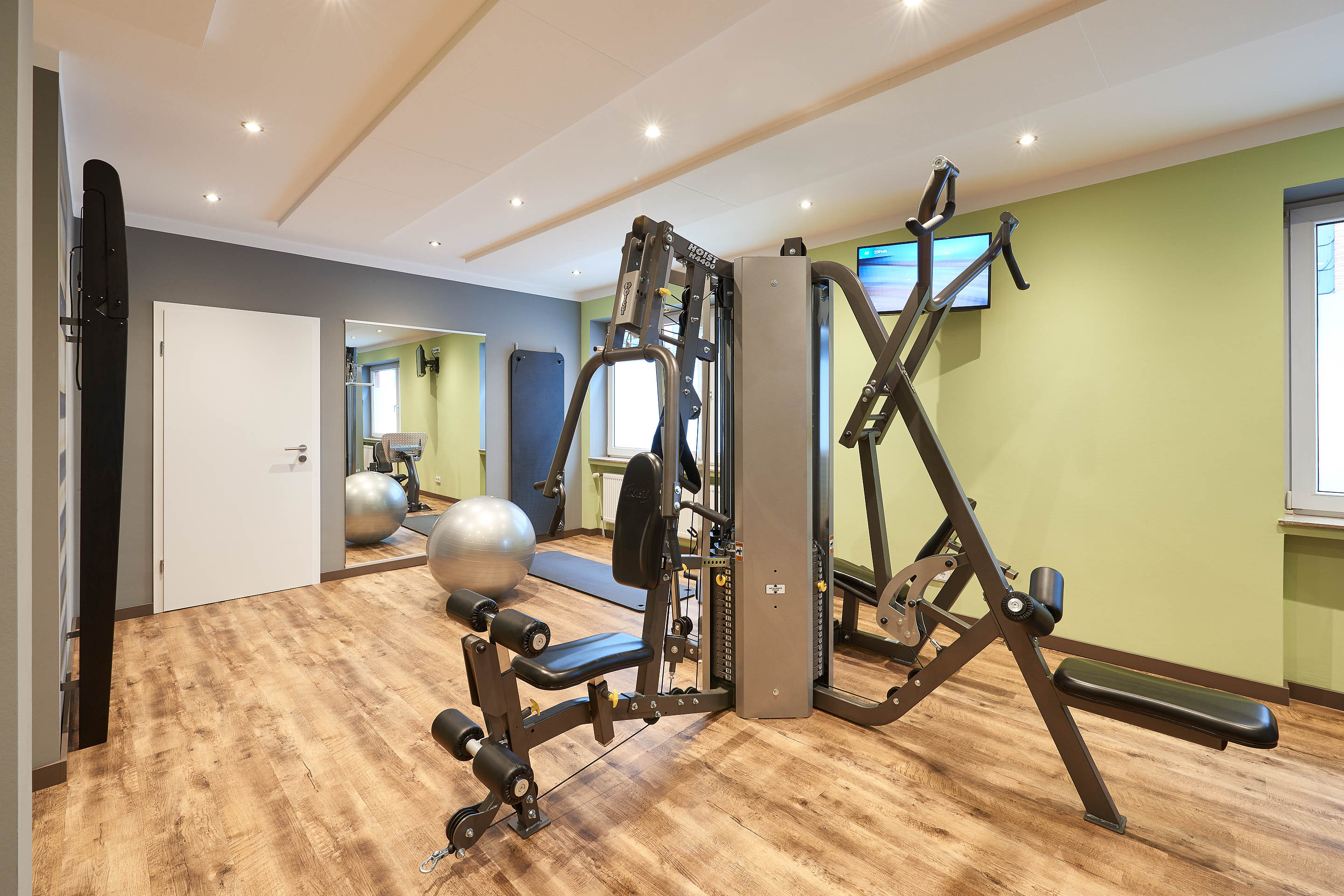 Fitnessraum mit Kraftgeräten, im Hintergrund Spiegel, Gymnastikball und Gymnastikmatten