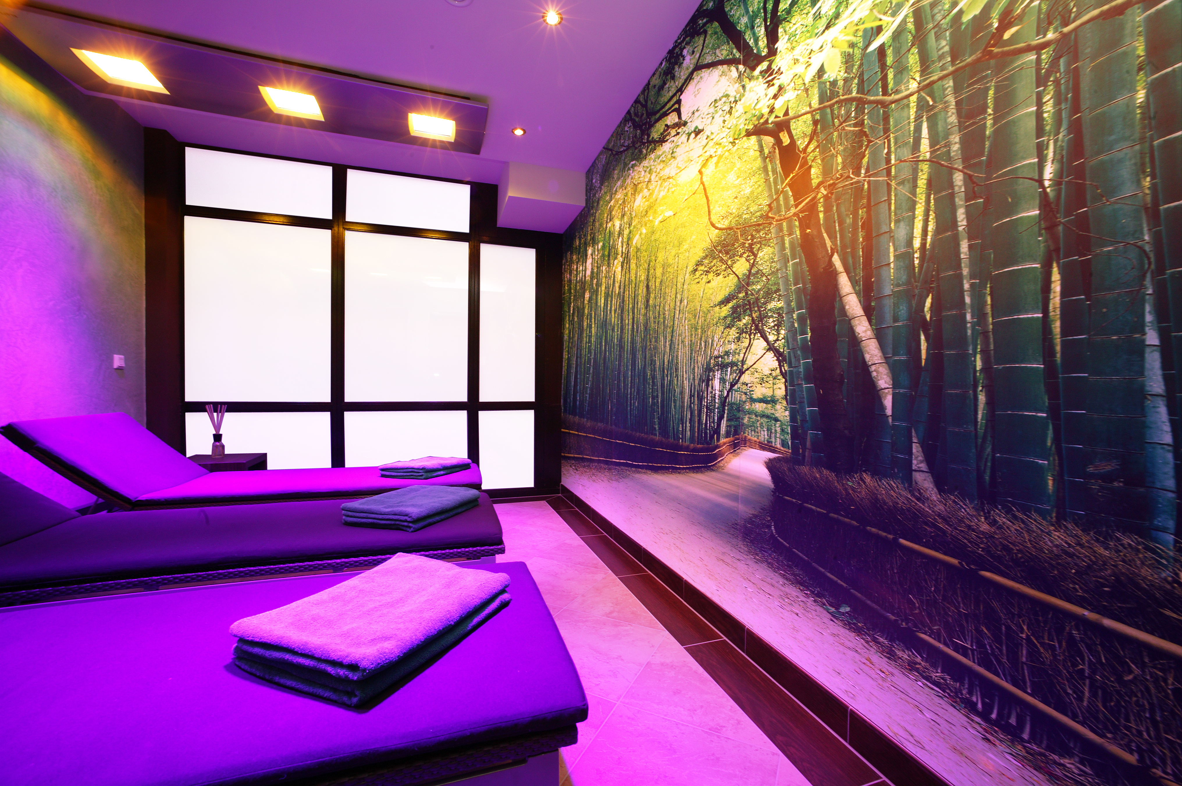 Klafs Sonnenraum im Wellnessbereich mit gemütlichen Liegen und Blick auf ein Wandbild mit Bambuswald